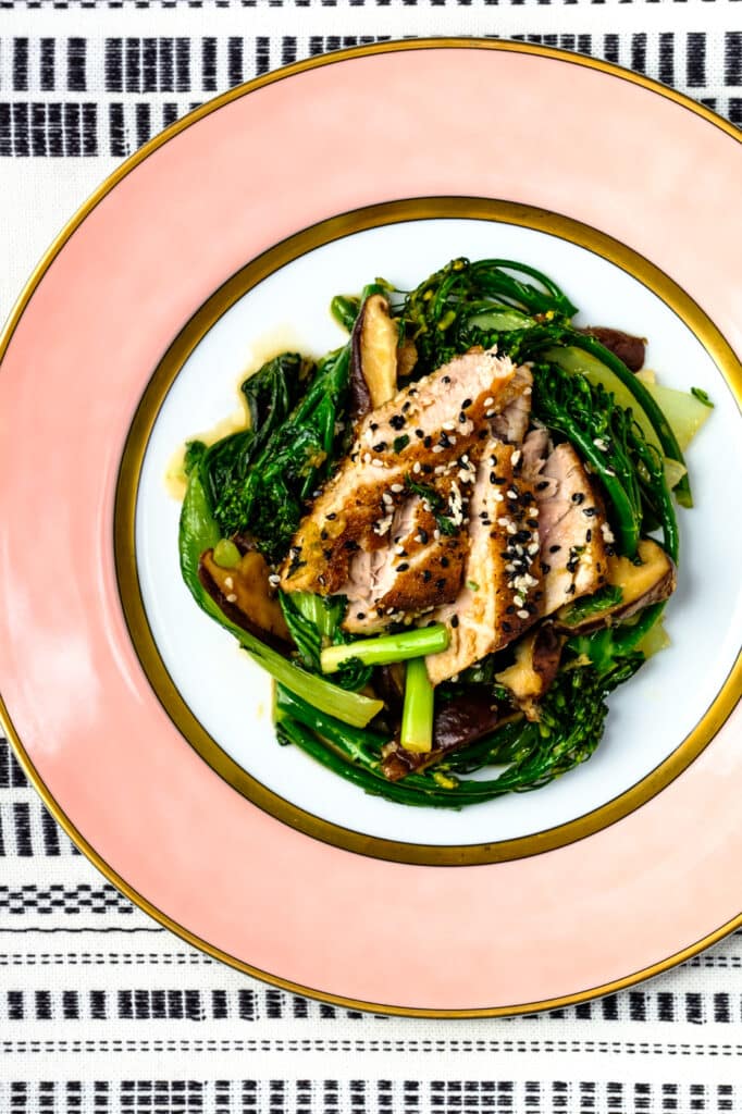bok choy, broccolini and mushroom stir fry, on a plate, topped with sliced of seared tuna