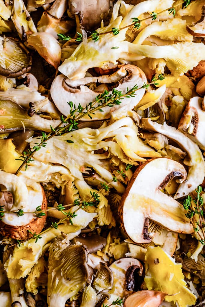 a variety of mushrooms, cut and arranged on a baking sheet, topped with fresh thyme