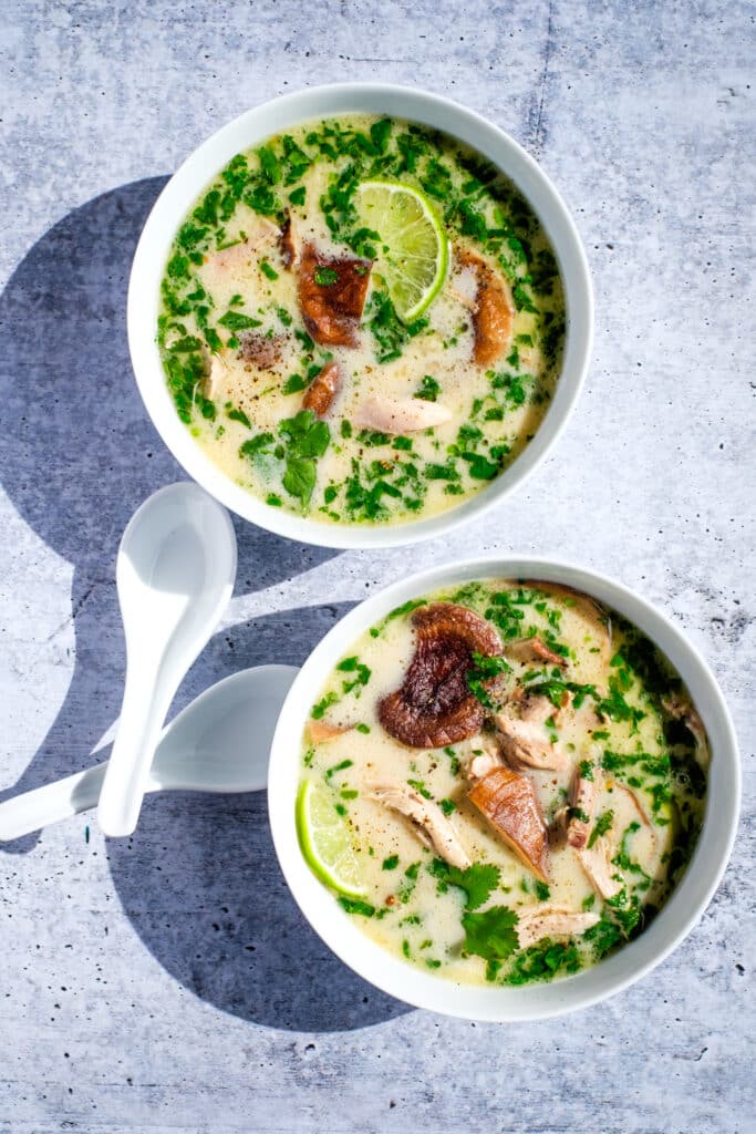 Two bowls of chicken coconut soup, with two spoons.