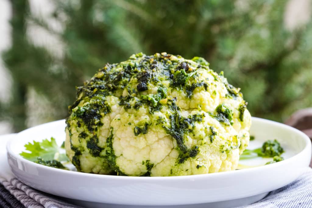 Whole roasted cauliflower with pesto on a plate