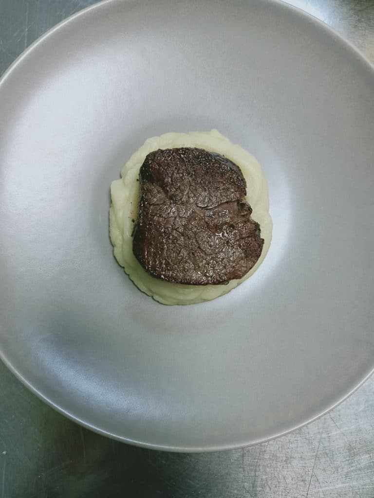 The cooked beef tenderloin steak on a plate. The meat is position on top of the puree.