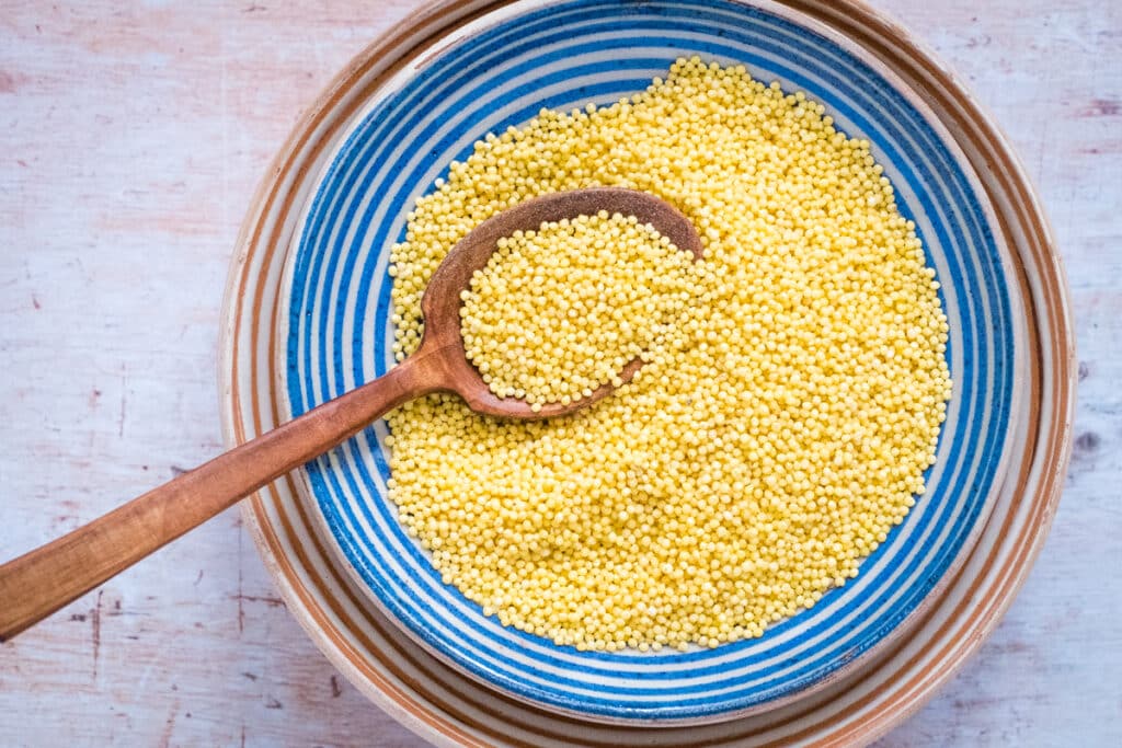 Millet grain in a bowl with a wooden spoon