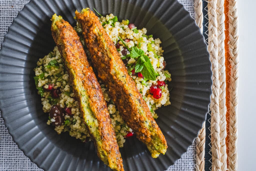 2 chicken kofta kebabs on top of millet tabbouleh, in a black plate