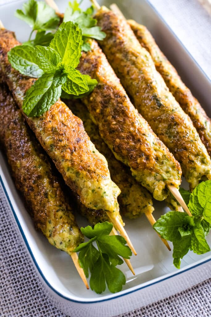 Chicken kofta skewers on a plate with mint