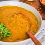 red lentil soup in a bowl, a wooden spoon, fresh cilantro