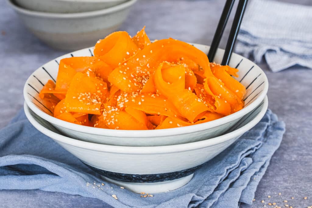 Carrot ribbon salad served in a bowl with chopsticks.