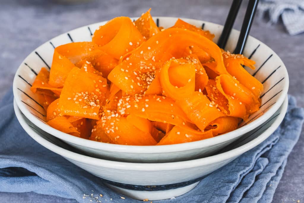 Carrot ribbon salad served in a bowl with chopsticks.