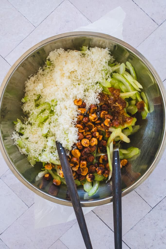 Sliced celery, grated Parmigiano Reggiano, roasted hazelnuts, and the dressing are combined in a large mixing bowl.