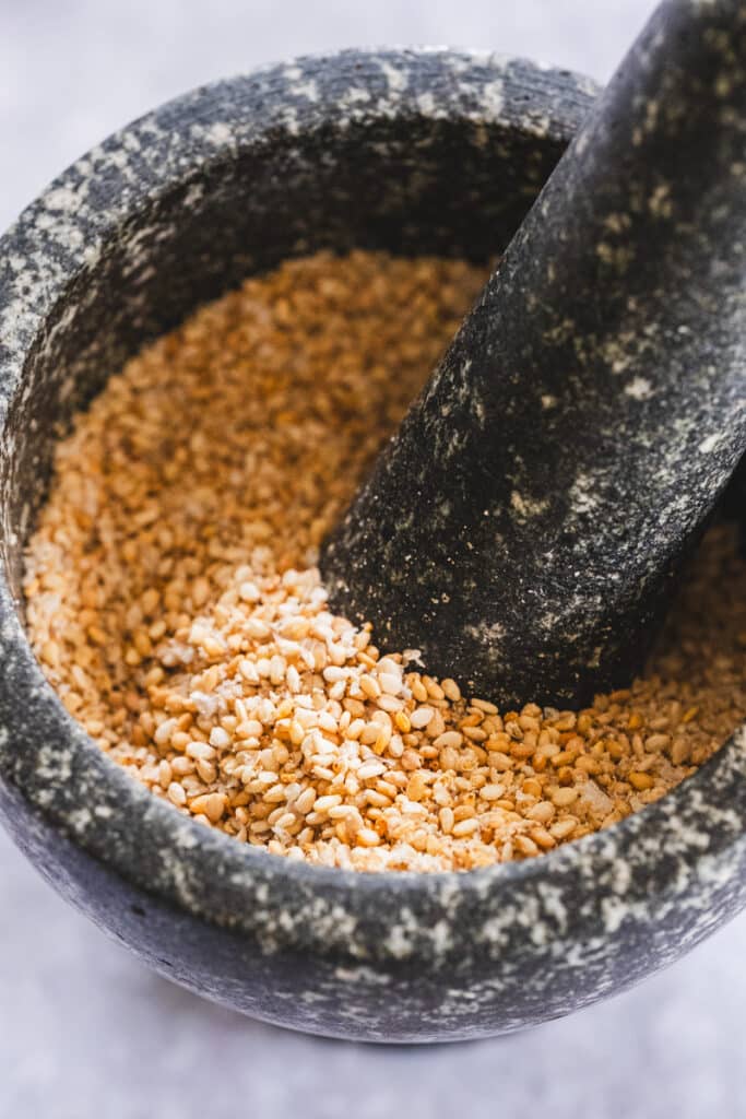 Using a mortar and pestle to crush the roasted semsame seeds and salt flakes.