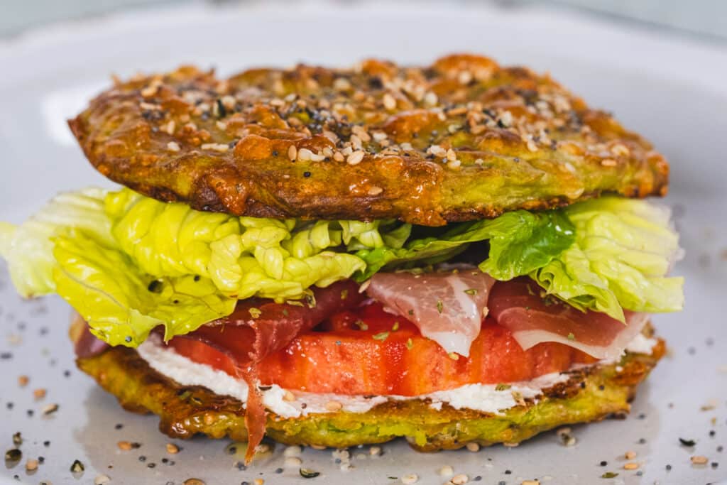 A sandwich made with avocado bread filled with cream cheese, tomatoes, prosciutto, and salad.