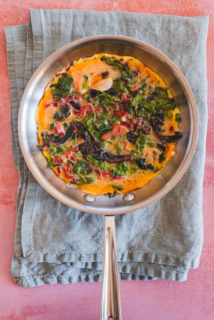 The Swiss chard frittata is in the stainless skillet and has been cooked on one side.