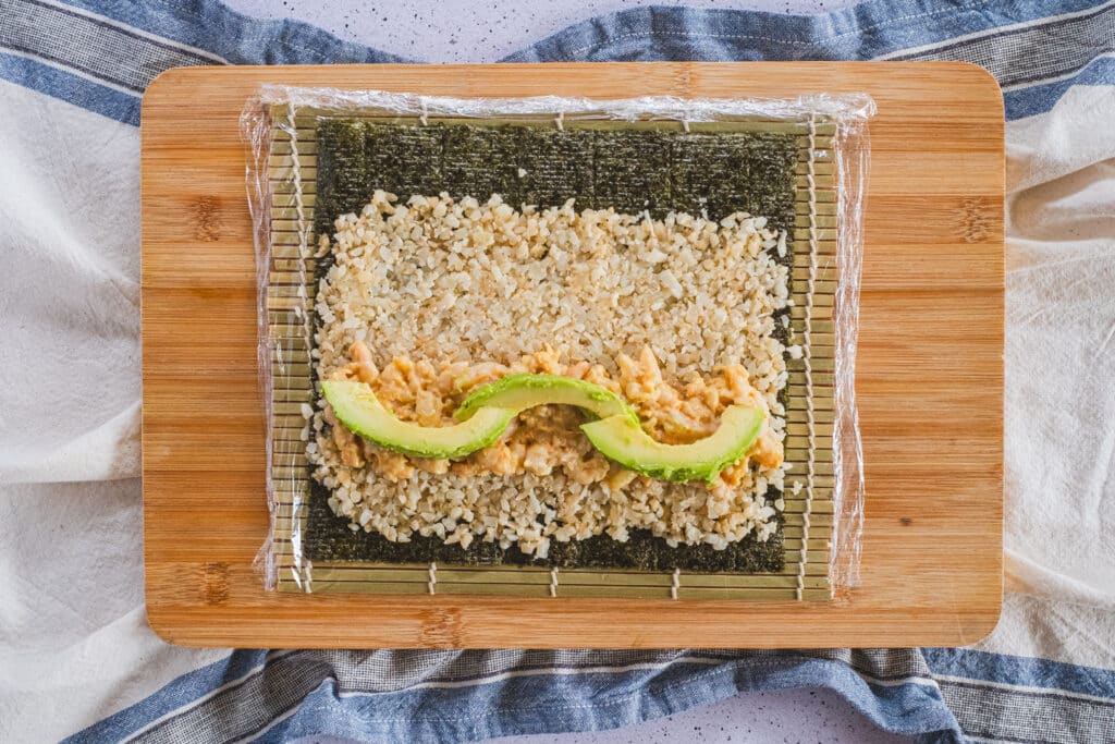 The nori sheet, filled with cauliflower rice, shrimp, and avocado, is ready to be rolled.
