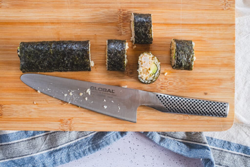 Slicing the sushi rolls on a cutting board using a very sharp knife.