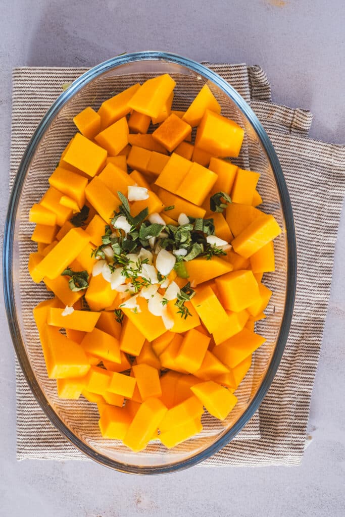 Cubed butternut squash with fresh herbs and garlic on a plate.