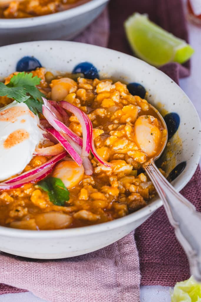 One serving of turkey pumpkin chili  topped with red onion, cilantro, and a dollop of crème fraîche.
