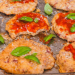 cottage cheese pizza bites on a baking sheet, topped with ketchup and basil leaves