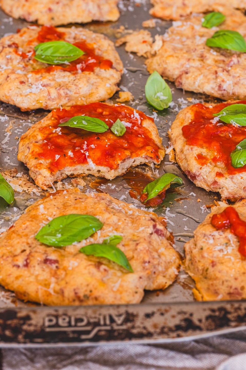 cottage cheese pizza bites on a baking sheet, topped with ketchup and basil leaves