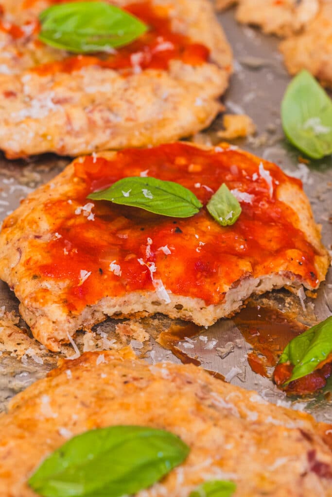 close up of cottage cheese pizza bites on a baking sheet, topped with ketchup and basil leaves