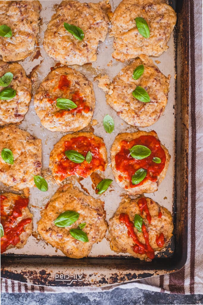 the pizza bites on a baking sheet, topped with ketchup and basil leaves