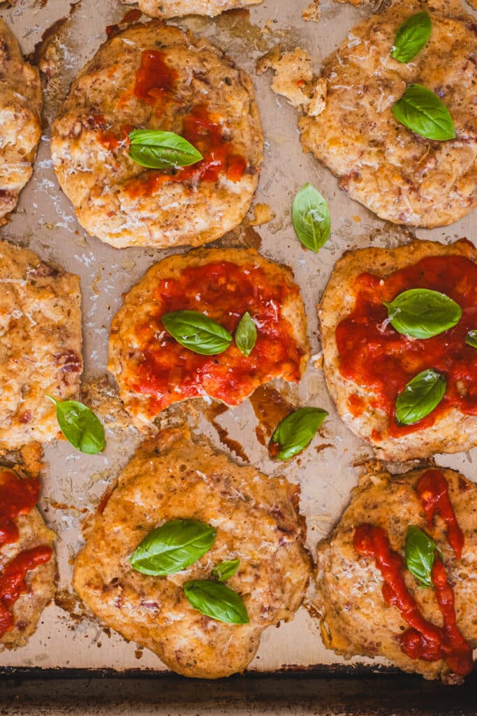 cottage cheese pizza bites on a baking sheet, topped with ketchup and basil leaves