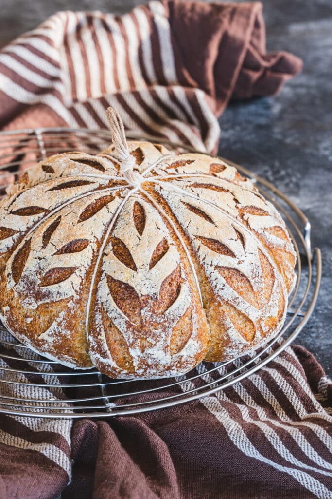 Freshly baked pumpkin shaped sourdough bread on a cooling rack.