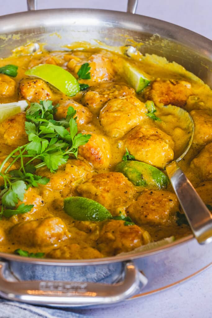 The coconut curry chicken meatballs in the pan garnished with fresh parsley and lime.