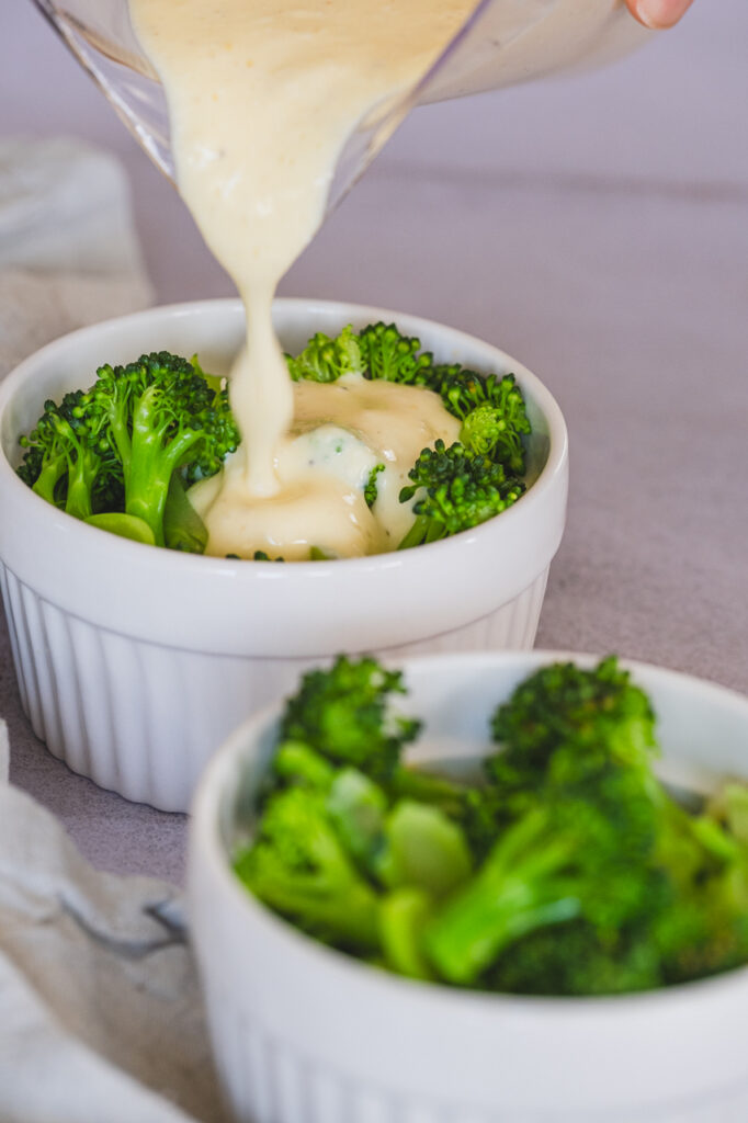 The custard is being poured over the broccoli in the ramekin.