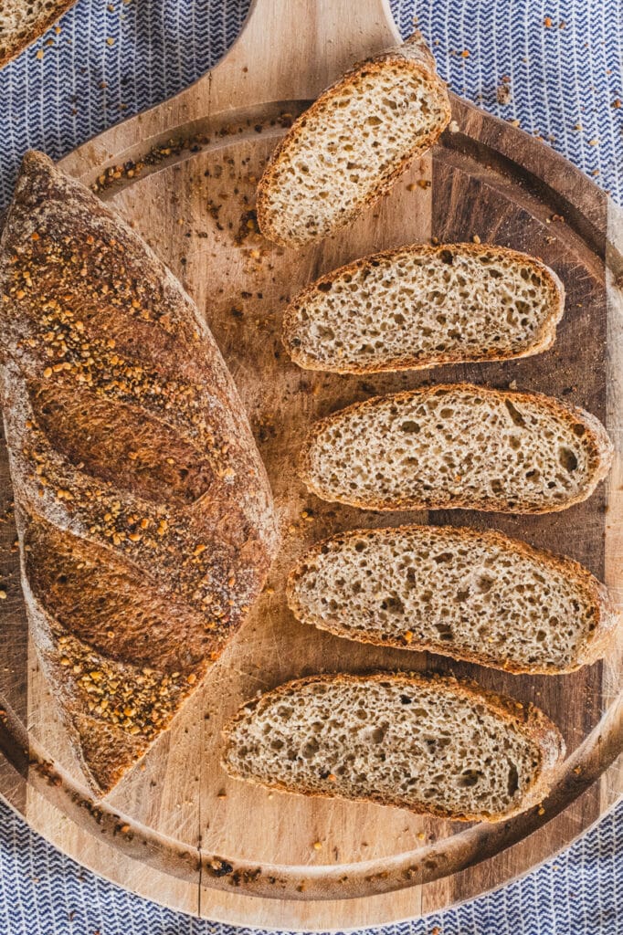 Slices of gluten-free sourdough baguette arranged on a wooden cutting board, showing the bread's airy crumb.
