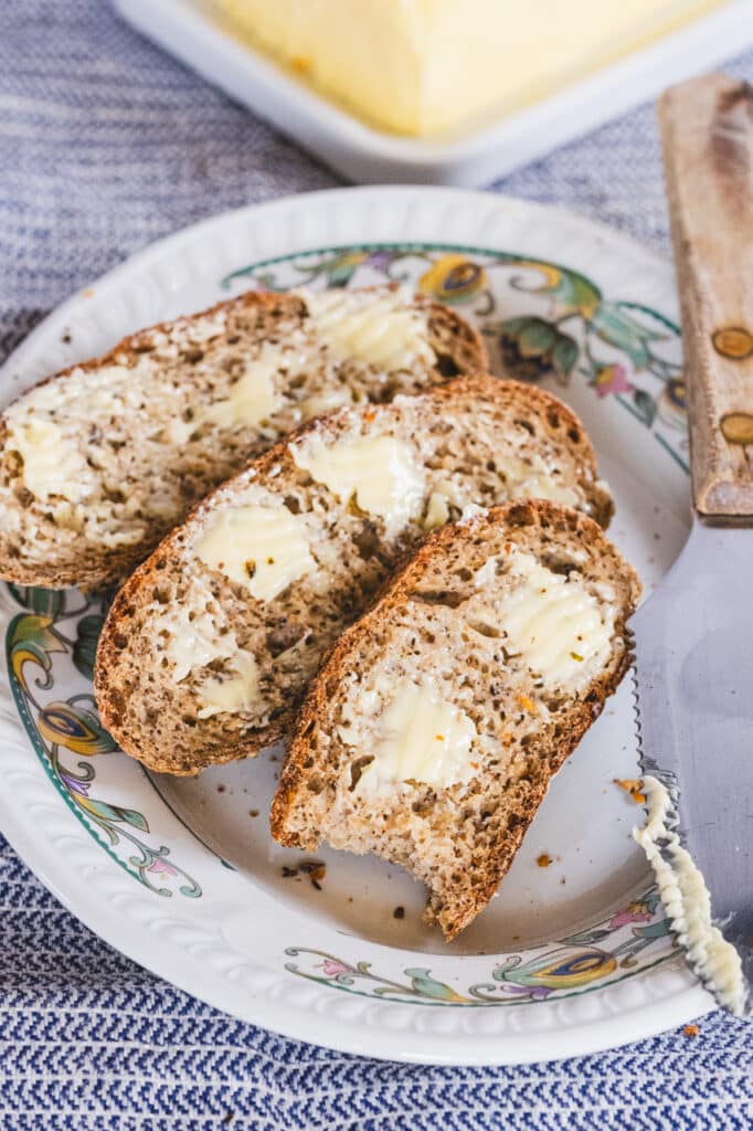 Three slices of gluten-free sourdough baguette with butter arranged on a white plate.