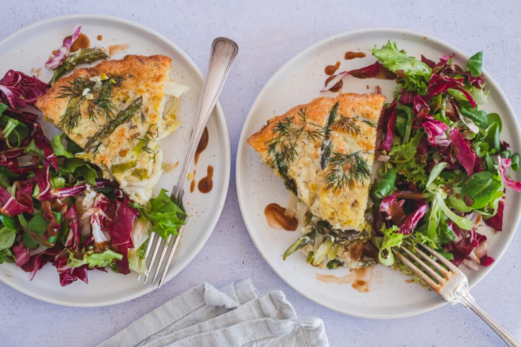 Two servings of crustless vegetable quiche, on two plates, next to a leafy greens salad