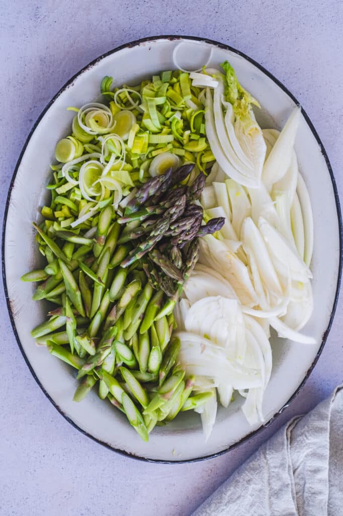 Clean, sliced leeks, fennel, and asparagus arranged neatly on a white plate.