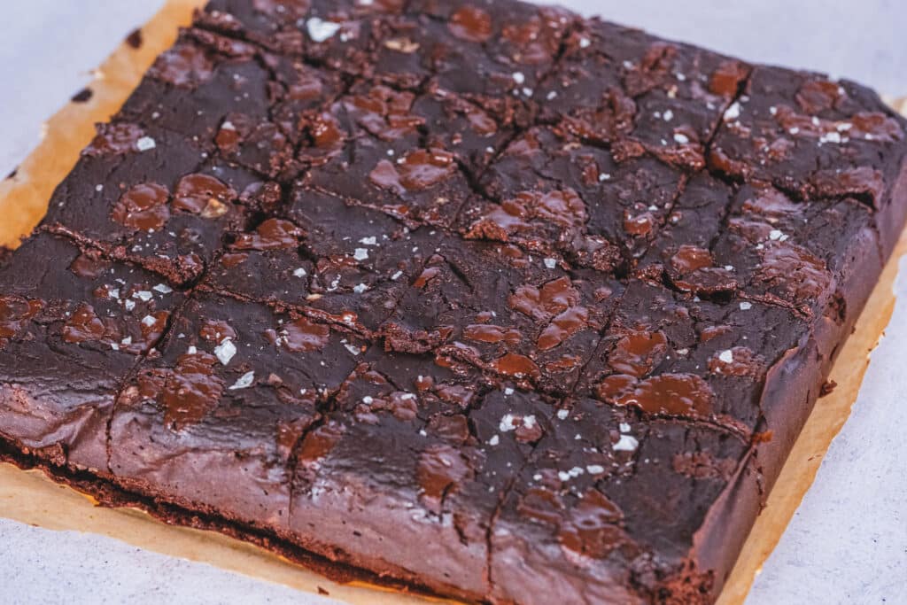 Freshly baked butternut squash brownies cut into neat squares, resting on a parchment-lined baking sheet.