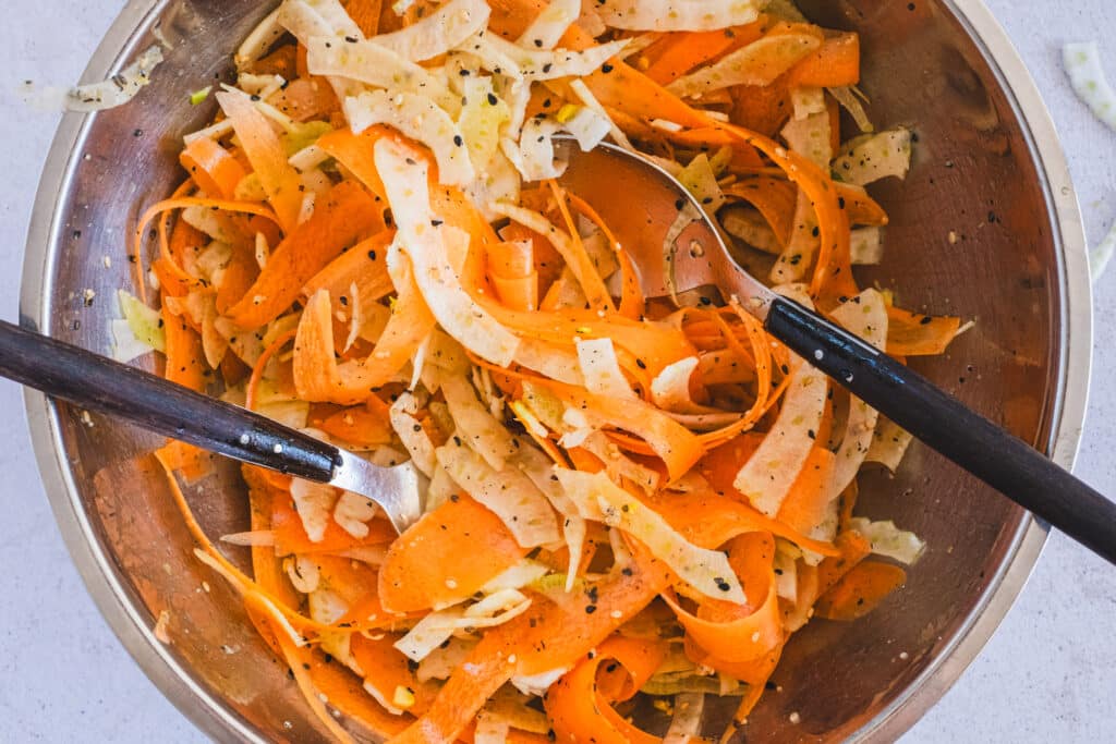 Tossing the carrot ribbons with the sliced fennel and the dressing in a mixing bowl.