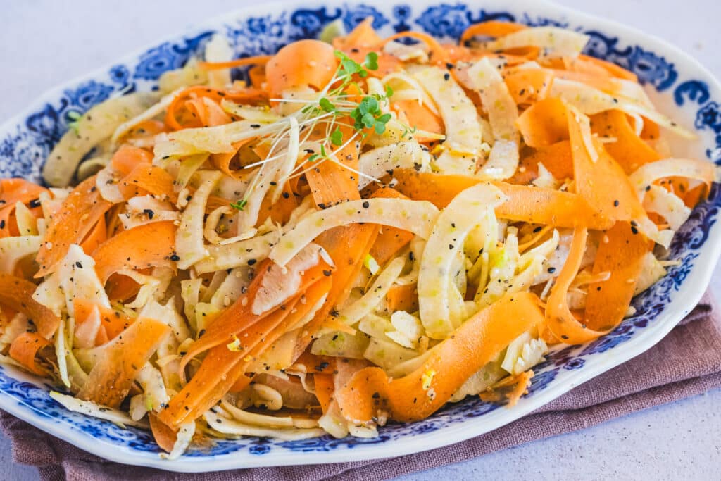 A plate of crunchy carrot and fennel salad, garnished with vibrant sesame lime dressing.