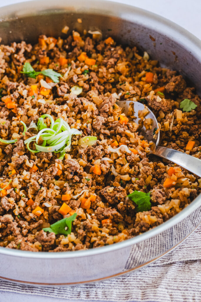 Cooked ground beef mixed with cauliflower rice in the pan, sprinkled with fresh green herbs on top.