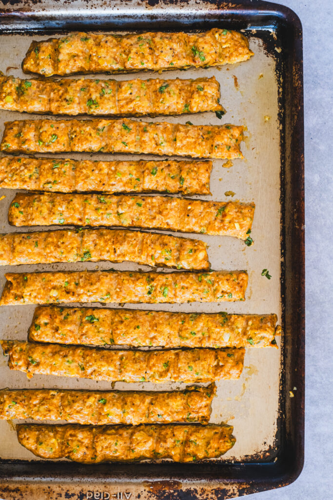 A baking sheet holding golden-brown chicken kebabs, cut into strips and freshly baked.