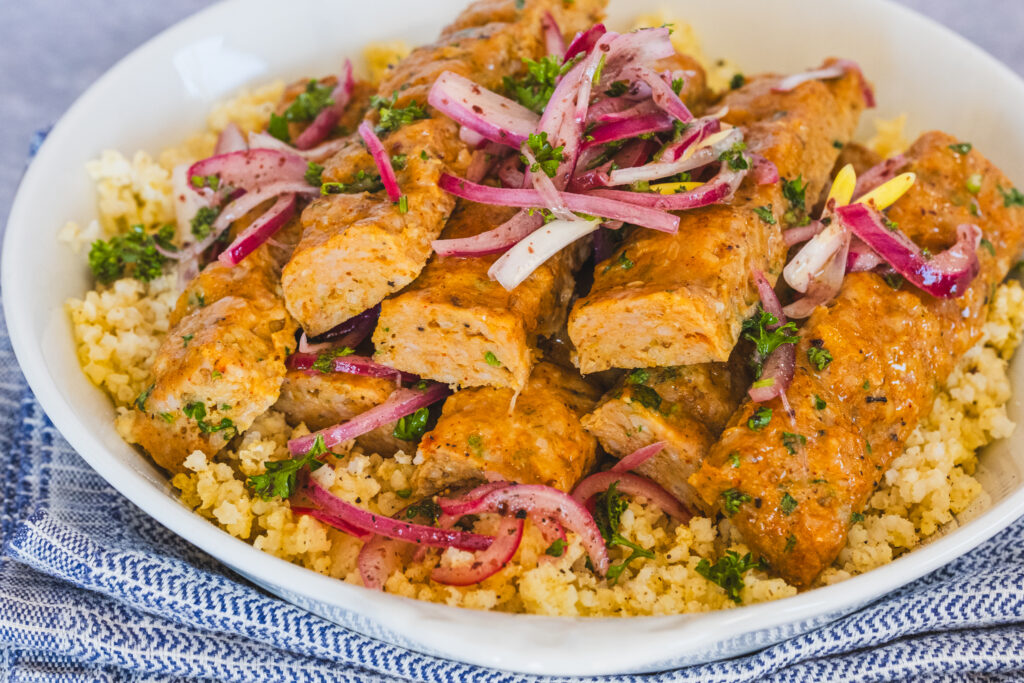 Sheet pan chicken kebabs arranged on a bed of fluffy millet, garnished with vibrant sumac onions.