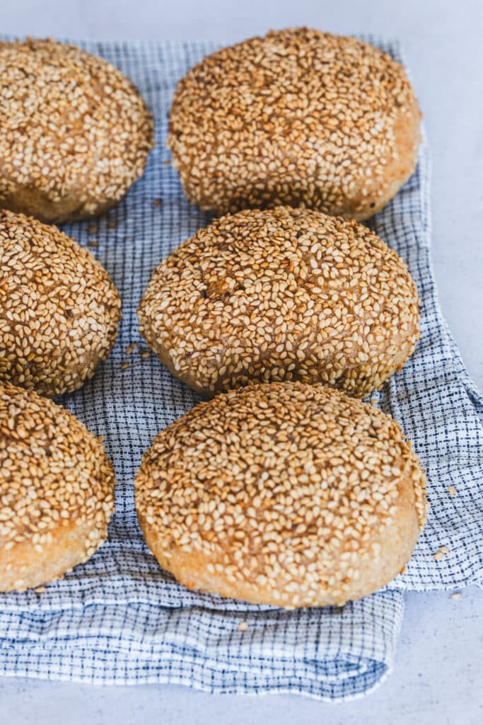 Six gluten-free sesame-crusted buns on a kitchen towel.