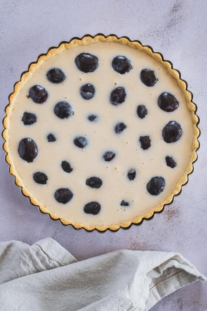 Gluten free tart crust filled with halved plums and custard, before baking