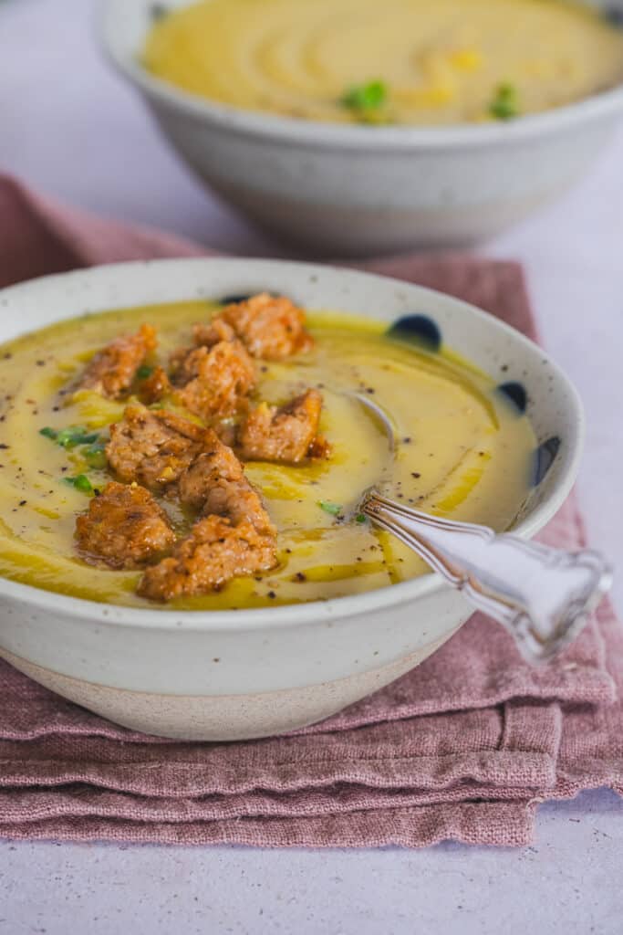 creamy red lentil and cauliflower soup, topped with chicken sausage, served in a bowl, with a spoon