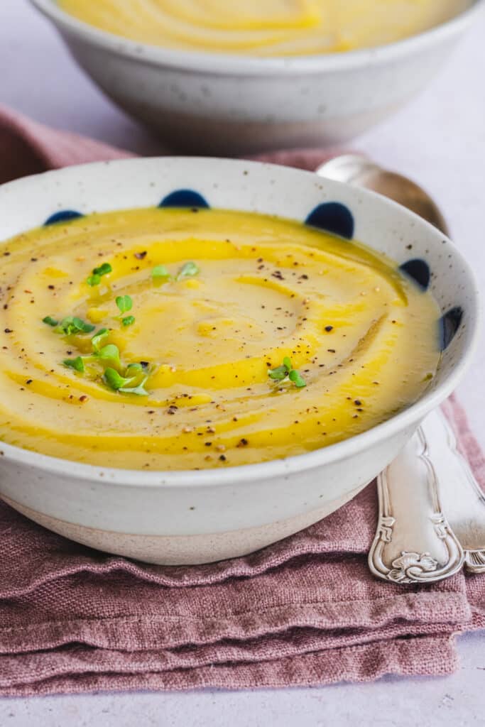 creamy red lentil and cauliflower soup served in a bowl, topped with broccoli microgreens