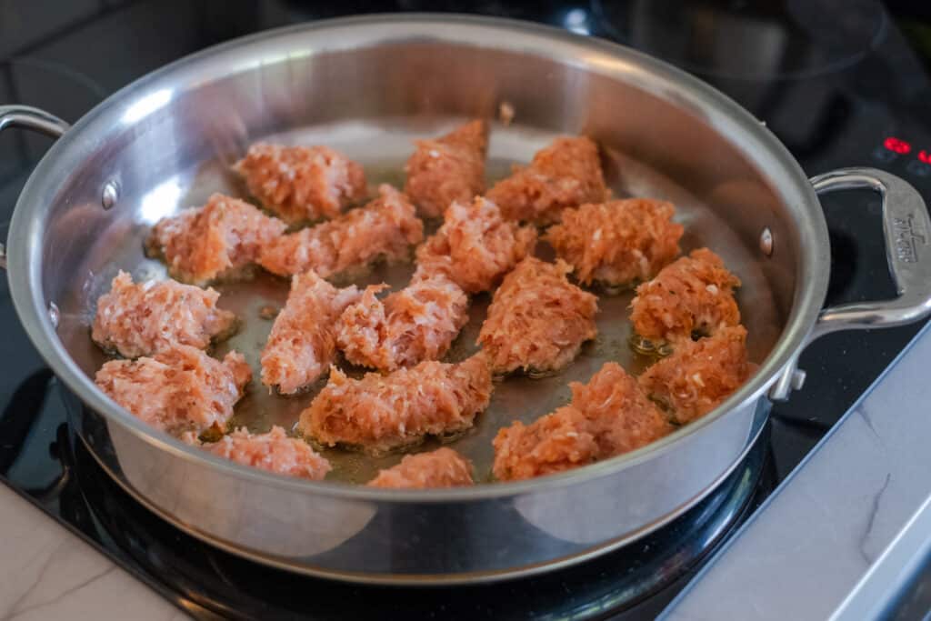 Italian chicken sausage clusters frying in olive oil, in a stainless steel pan