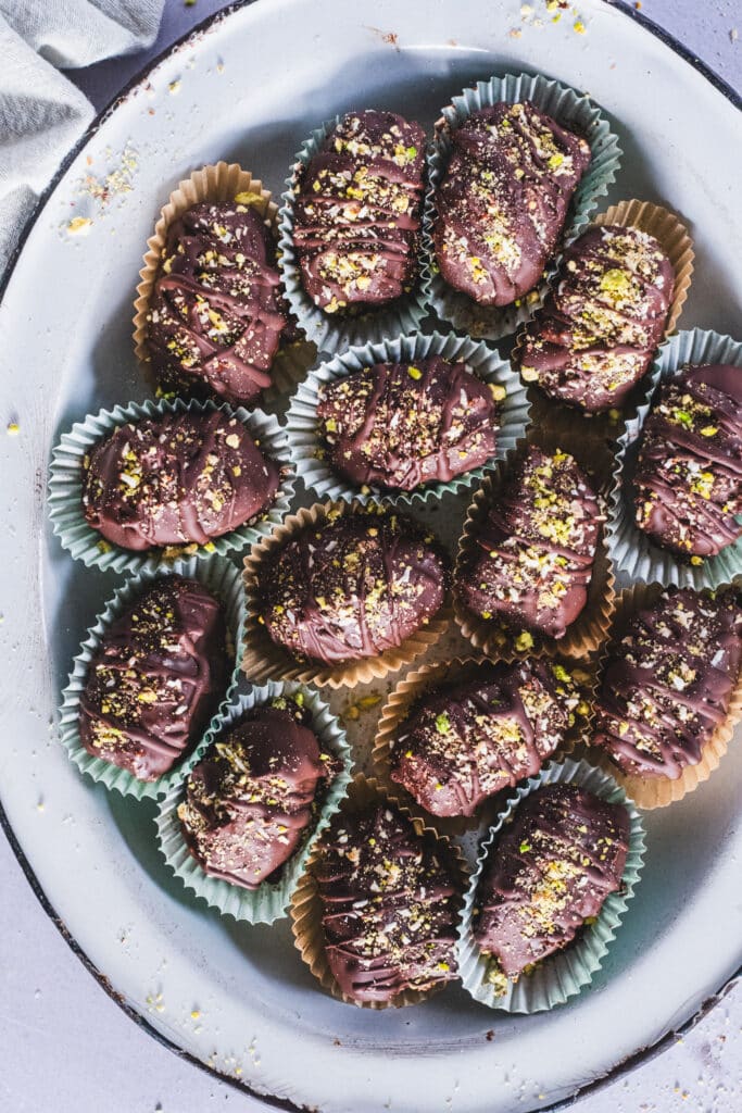 Tâmaras de chocolate Dubai colocadas em forminhas de papel para mini muffins, cuidadosamente dispostas em um prato.